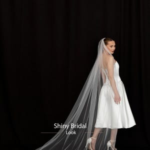 May include: A bride in a white satin wedding dress and long veil. The veil is trimmed with small beads and trails behind the bride. The text "Shiny Bridal Look" is visible in the image.