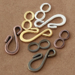 May include: A collection of metal jewelry clasps in various finishes, including gold, silver, bronze, and copper. The clasps feature a figure-eight design and a hook closure, suitable for necklaces and bracelets.