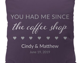 Puede incluir: Cojín de color morado con el texto "YOU HAD ME SINCE the coffee shop" en blanco con una fila de pequeños corazones blancos debajo del texto. Los nombres "Cindy & Matthew" y la fecha "June 19, 2019" están impresos debajo de los corazones.
