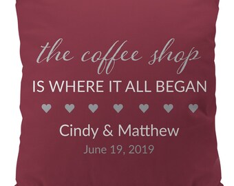 Puede incluir: Una almohada de color burdeos con texto blanco que dice "the coffee shop is where it all began" con una fila de cinco corazones grises debajo del texto. Debajo de los corazones está el texto "Cindy & Matthew" y "June 19, 2019".