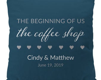 Puede incluir: Cojín de sofá azul turquesa con texto blanco que dice "THE BEGINNING OF US the coffee shop" con seis corazones blancos y los nombres "Cindy & Matthew" y la fecha "June 19, 2019".