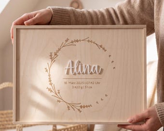 May include: A rectangular light-colored wooden plaque featuring a laser-engraved floral wreath design. The name Alina is displayed in raised white script lettering. Below the name, the text reads 18, März 2025 | 07:42 Uhr, 3.420 g | 51 cm.
