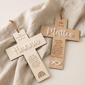 Könnte beinhalten: Zwei Holzkreuze mit weißer Schrift und Lederschlaufen. Auf dem einen Kreuz steht "Hanna" und "Zur Kommunion 26.04.2026". Auf dem anderen steht "Matteo" und "Zur Taufe 15.03.2026". Beide haben zusätzlichen Text.