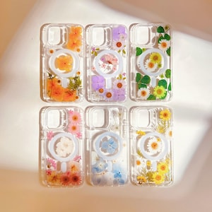 May include: Six clear phone cases with a ring holder. Each case features a different pressed flower design, including orange, purple, yellow, pink, blue, and white flowers.