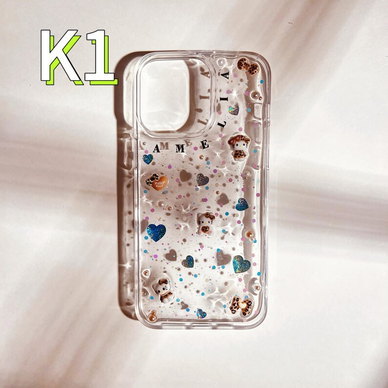May include: A clear phone case with a glittery liquid inside. The case has a design of small hearts, stars, and a small animal figure. The text "Amelia" is printed on the back of the case.