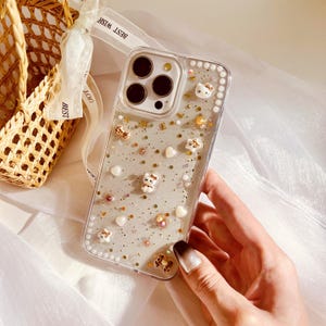Puede incluir: Una funda transparente para tel&eacute;fono con un fondo brillante y peque&ntilde;as figuritas de animales blancas. La funda tiene un borde elevado de peque&ntilde;as perlas blancas.