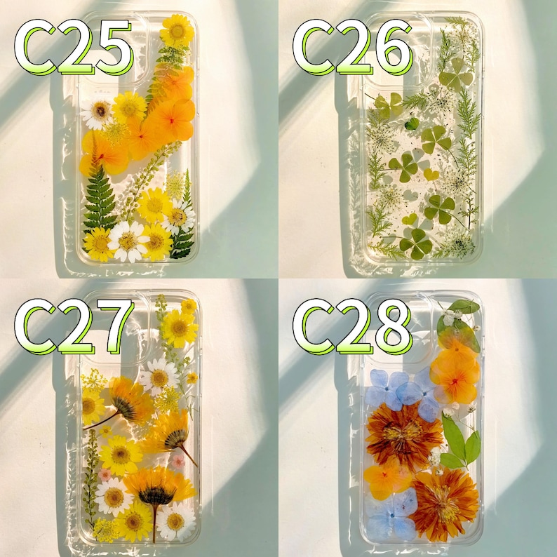 Op de afbeelding: Vier transparante telefoonhoesjes met geperste bloemen. De hoesjes hebben gele, witte en oranje bloemen en groene bladeren. Elk hoesje heeft een ander bloemarrangement, waaronder madeliefjes, zonnebloemen en klavers met vier blaadjes. De hoesjes zijn gelabeld met C25, C26, C27 en C28.