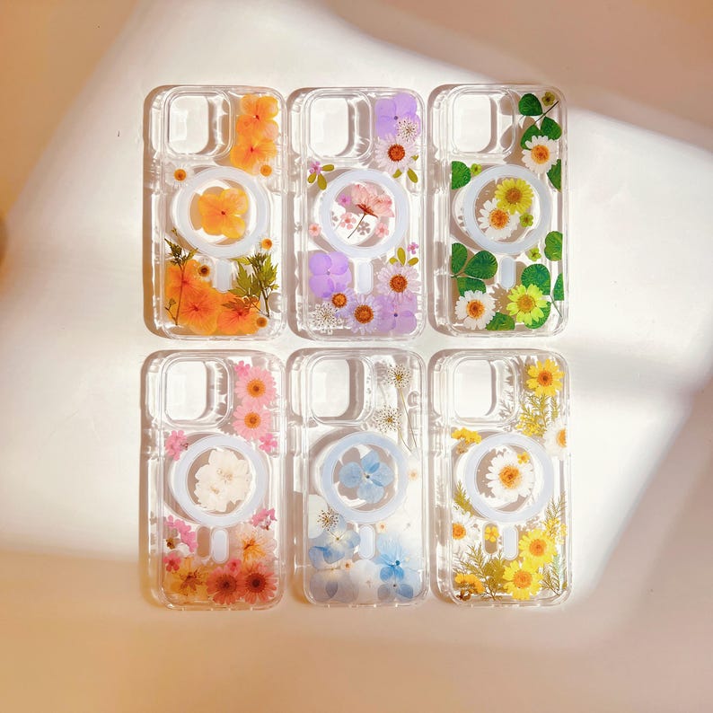 May include: Six clear phone cases with a ring holder. Each case features a different pressed flower design, including orange, purple, yellow, pink, blue, and white flowers.