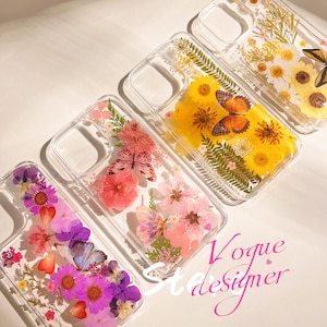 May include: Clear phone cases with pressed flowers and butterflies. The cases feature a variety of colorful flowers, including pink, purple, and yellow, and butterflies. The cases are arranged on a white surface.