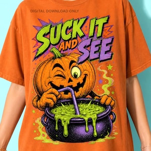 Op de afbeelding: Een oranje t-shirt met een afbeelding van een knipogende pompoen die met een rietje groene vloeistof uit een paarse ketel drinkt. De tekst "SUCK IT AND SEE" en "DIGITAL DOWNLOAD ONLY" staat in gestileerde groene en paarse letters.