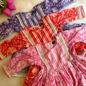 May include: Three girls' dresses in pink, red, and purple with floral patterns and white lace trim. The dresses have a striped bodice and a gathered skirt.