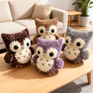 May include: Four handmade crochet owl plush toys in shades of brown, purple, and gray, with cream-colored bellies and large black eyes. The owls are displayed on a light brown wooden table, showcasing their soft, textured appearance.