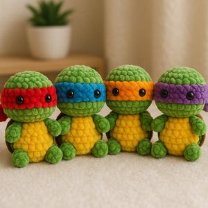 May include: Four handmade crochet turtle toys. Each turtle has a green head and limbs, a yellow shell, and a coloured headband: red, blue, orange, and purple. The turtles are sitting on a cream-coloured surface.