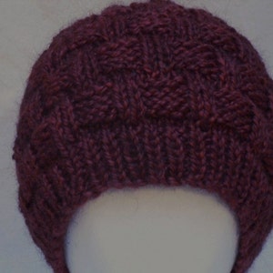 May include: A dark purple knitted hat with a cable knit pattern.