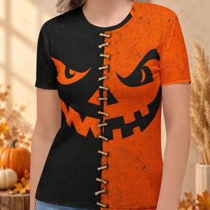 May include: A short-sleeve t-shirt featuring a split design with a black left side and an orange right side. A graphic of a jack-o'-lantern face is printed across both halves, with a vertical row of faux stitching running down the centre.