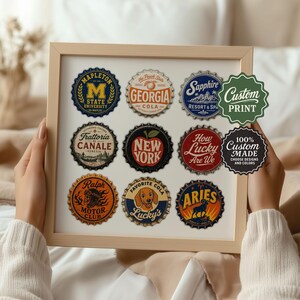 May include: A framed print showcasing nine bottle cap designs with diverse logos and text. The caps feature phrases like "Georgia Cola," "New York," and "Lucky's Favorite Cola." The frame also includes two stickers that say "Custom Print" and "100% Custom Made."