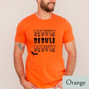 May include: Orange t-shirt with a black bat and the text "DAD-VULA" repeated three times.