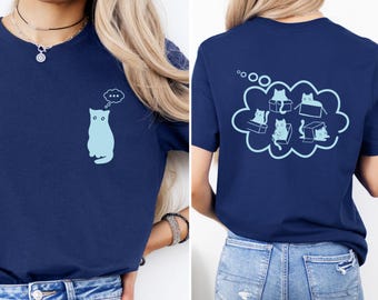 May include: Navy blue t-shirt featuring a light blue cat silhouette with a thought bubble on the front. The back of the shirt displays a light blue cloud with cat illustrations. The shirt is a casual wear item.