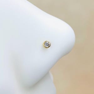 Könnte beinhalten: Ein goldener Nasenring mit einem klaren, runden Edelstein.