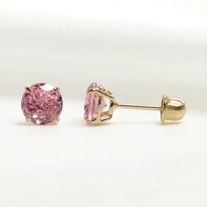 Puede incluir: Un par de pendientes de botón con gemas rosas redondas y facetadas engastadas en metal dorado. Un pendiente está en posición vertical, el otro de lado, mostrando el poste y el cierre.