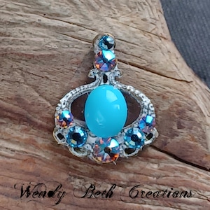 May include: A silver pendant with a turquoise cabochon stone surrounded by iridescent blue and orange rhinestones.