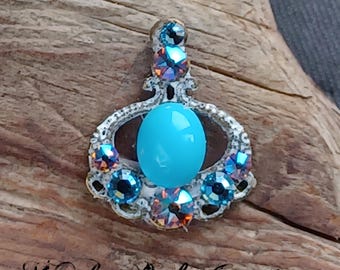 May include: A silver pendant with a turquoise cabochon stone surrounded by iridescent blue and orange rhinestones.