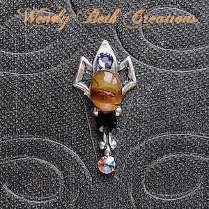 May include: A silver pendant with a tiger's eye stone, a purple crystal, and a black crystal. The pendant is in the shape of a flower.