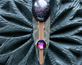 May include: A handcrafted pendant featuring a dark blue, speckled stone cabochon at the top, a copper-colored metal accent, and a vibrant pink gemstone at the bottom. The pendant is set against a dark, textured background. The text "Wendy Beth Creations" is at the bottom.