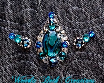 May include: A teal blue gemstone surrounded by smaller blue rhinestones in a silver setting. The gemstone is set in a teardrop shape and is surrounded by a silver filigree design. The piece is part of a set of three, with two smaller pieces featuring blue rhinestones.