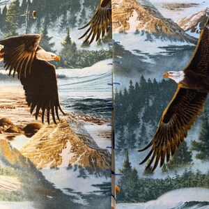 K&ouml;nnte beinhalten: Doppelseitige Ansicht eines Journals oder Notizbuchs mit einem gedruckten Design, das Wei&szlig;kopfseeadler zeigt, die &uuml;ber einer Berglandschaft fliegen. Das Cover hat ein blau-gr&uuml;nes Farbschema mit einer schneebedeckten Bergkette und immergr&uuml;nen B&auml;umen.