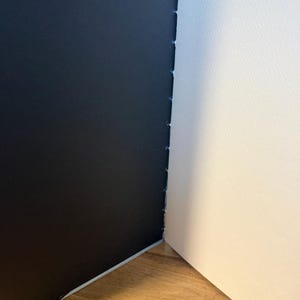 K&ouml;nnte beinhalten: Ein offenes Skizzenbuch mit schwarzem Einband und wei&szlig;en Seiten. Die Seiten sind mit blauem Faden gebunden. Das Skizzenbuch liegt auf einer Holzoberfl&auml;che.