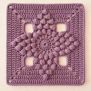 Puede incluir: Un motivo cuadrado de ganchillo en color morado polvoriento. El diseño presenta un patrón circular central compuesto por puntos de garbanzo, rodeado por cuatro aberturas cuadradas y un borde sólido de puntos altos que forma la figura.