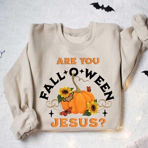 May include: A beige sweatshirt with the text "Are you Fall-o-ween Jesus?" printed on the front. The text is surrounded by a pumpkin, sunflowers, and butterflies.