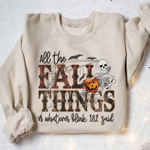 May include: A beige sweatshirt with a graphic print of a skeleton holding a pumpkin and the text "All the Fall Things or whatever blink 182 said".