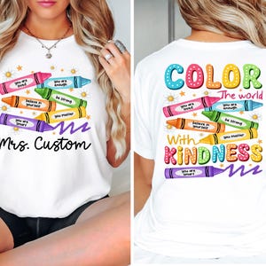 K&ouml;nnte beinhalten: Wei&szlig;es T-Shirt mit einem bunten Buntstift-Design. Die Vorderseite zeigt Buntstifte mit positiven Botschaften und dem Text "Mrs. Custom". Auf der R&uuml;ckseite steht "COLOR the world with KINDNESS" mit weiteren Buntstiften und ermutigenden S&auml;tzen.