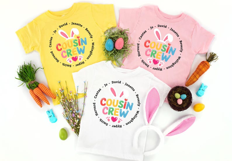 May include: Three children's t-shirts in yellow, pink, and white, each printed with "COUSIN CREW" in a circle design with bunny ears and hearts. Easter decorations include carrots, eggs, and a bunny ear headband.