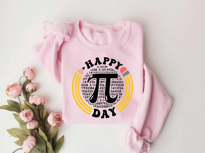 May include: A pink sweatshirt with a graphic design of a large black pi symbol surrounded by yellow and orange pencils. The text "Happy Pi Day" is written above and below the pi symbol. The pi symbol is surrounded by numbers.