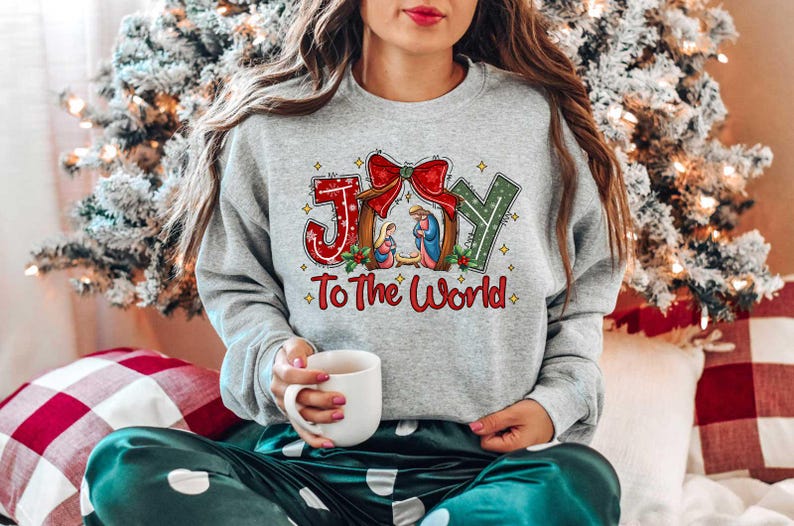 May include: A gray sweatshirt with a Christmas-themed design featuring the words "Joy to the World" and a depiction of the nativity scene. The design includes a red bow and green holly.