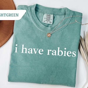 Może przedstawiać: Jasnozielony t-shirt z nadrukiem "i have rabies" w kolorze białym na przodzie.