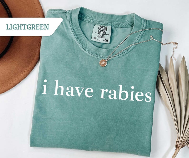 Może przedstawiać: Jasnozielony t-shirt z nadrukiem "i have rabies" w kolorze białym na przodzie.