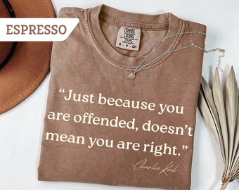 May include: Espresso-colored t-shirt with the quote "Just because you are offended, doesn't mean you are right." in white lettering. A silver necklace with a pendant rests on the shirt. The shirt is from Comfort Colors.