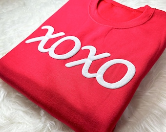 May include: A red t-shirt with the word "XOXO" printed in white on the front.