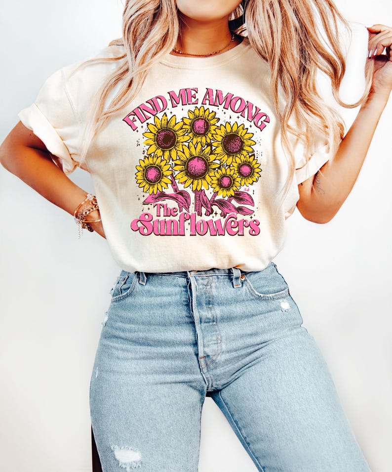 May include: A cream colored t-shirt with a graphic of sunflowers and the text "Find me among the sunflowers" in pink.