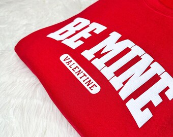 May include: Red sweatshirt with white text that reads "Be Mine Valentine".