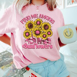 May include: Pink t-shirt with a graphic of sunflowers and the text "Find Me Among The Sunflowers".
