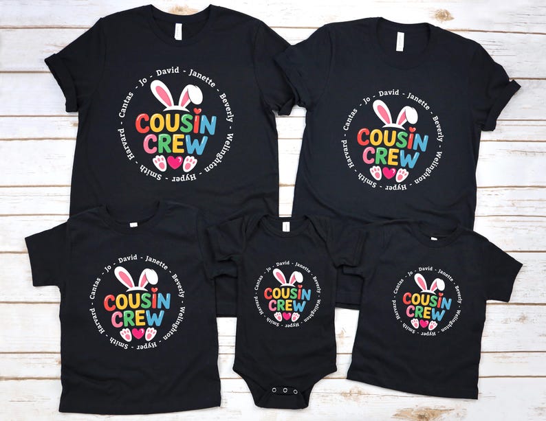 May include: Black t-shirts with the text "COUSIN CREW" in a colourful design, featuring bunny ears and hearts. The shirts are available in various sizes, including a onesie. Names are printed around the design.