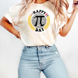 May include: A white t-shirt with a graphic of a black pi symbol surrounded by yellow and orange circles. The graphic also includes the text "HAPPY PI DAY" and a series of numbers.