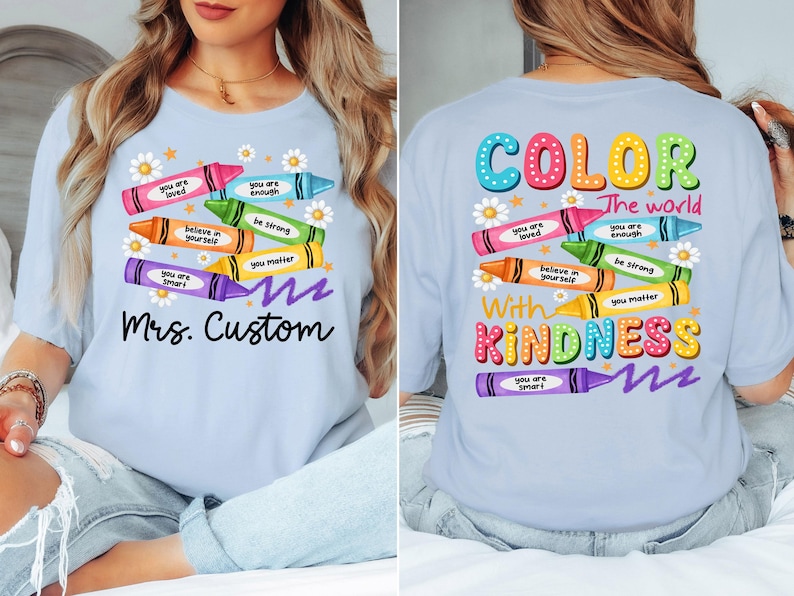 K&ouml;nnte beinhalten: Hellblaues T-Shirt mit bunten Buntstift-Grafiken und positiven Botschaften. Auf der Vorderseite steht "Mrs. Custom", auf der R&uuml;ckseite "Color the world with kindness".