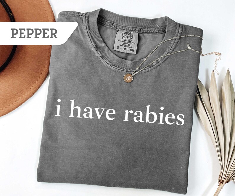Może przedstawiać: Szary T-shirt z nadrukiem "i have rabies" w kolorze białym. Koszulka wykonana jest z miękkiego, wygodnego materiału i ma luźny kr&oacute;j.