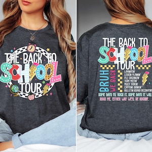 May include: Dark gray t-shirt with a colorful "The Back to School Tour" graphic. The design includes a clock, globe, apple, and pencil. The back of the shirt has text that says "Bruh We Back" and a list of school-related activities.